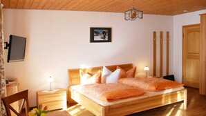 Un dormitorio con techo de madera, una cama con ropa de cama naranja, una mesita de noche con una lámpara, un cuadro en la pared y un televisor montado en la pared.