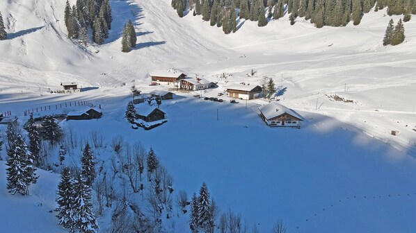 A snow-covered mountain area with several buildings, including cabins and a lodge, surrounded by trees.