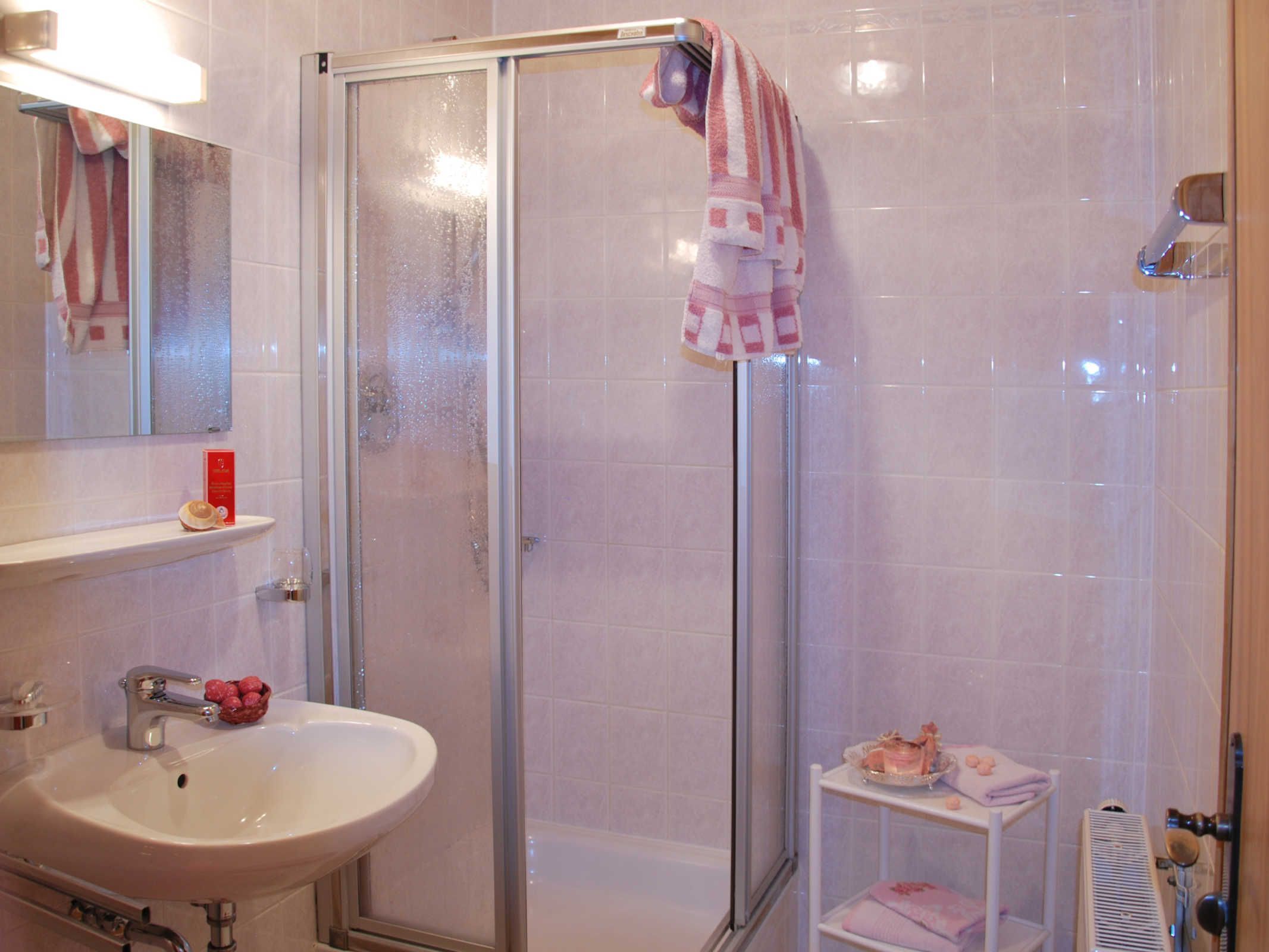 Un baño con cabina de ducha de vidrio, un lavabo blanco y un pequeño estante con una caja roja y un objeto decorativo.