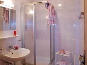Une salle de bain avec une douche à parois de verre, un lavabo blanc et une petite étagère sur laquelle se trouvent une boîte rouge et un objet décoratif.