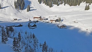 Une zone montagneuse enneigée, avec plusieurs bâtiments, dont des chalets et un refuge, le tout entouré d’arbres.
