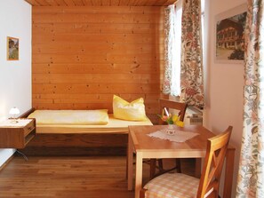 Een gezellige kamer met een houten wand, een bed met geel beddengoed, een houten tafel met een stoel en een raam met bloemen gordijnen.