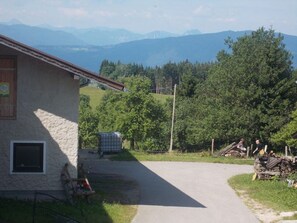 Una edificación rural con fachada de piedra, un camino de entrada pavimentado y vistas a montañas.