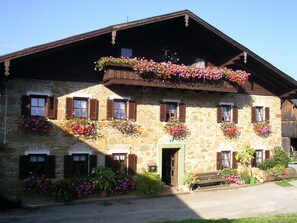 Un edificio de piedra con varias ventanas, algunas con contraventanas y balcones con flores.