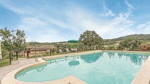 Une piscine à bord incurvé, entourée d’une clôture, d’où l’on peut admirer des collines et des arbres en arrière-plan.