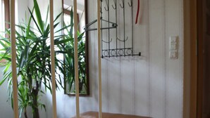 Um quarto com um banco de madeira, uma planta em vaso, um cabide de parede e uma porta.