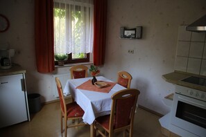 Eine kleine Küche mit Tisch, Stühlen, einer Kaffeemaschine und einem Fenster mit Vorhängen.