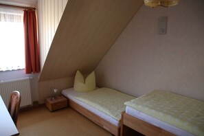 A small, single-bed room with a sloped ceiling, a bedside table with a lamp, and a window with curtains. - Apartment Blosenburgblick (Erfurt)