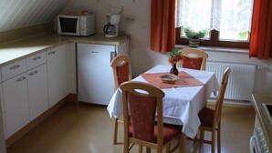 Uma cozinha compacta com uma mesa de jantar, cadeiras, micro-ondas, máquina de café e um relógio na parede.
