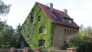 A house with a sloped roof, covered partially in ivy, and a stone fence in front. - Apartment Blosenburgblick (Erfurt)
