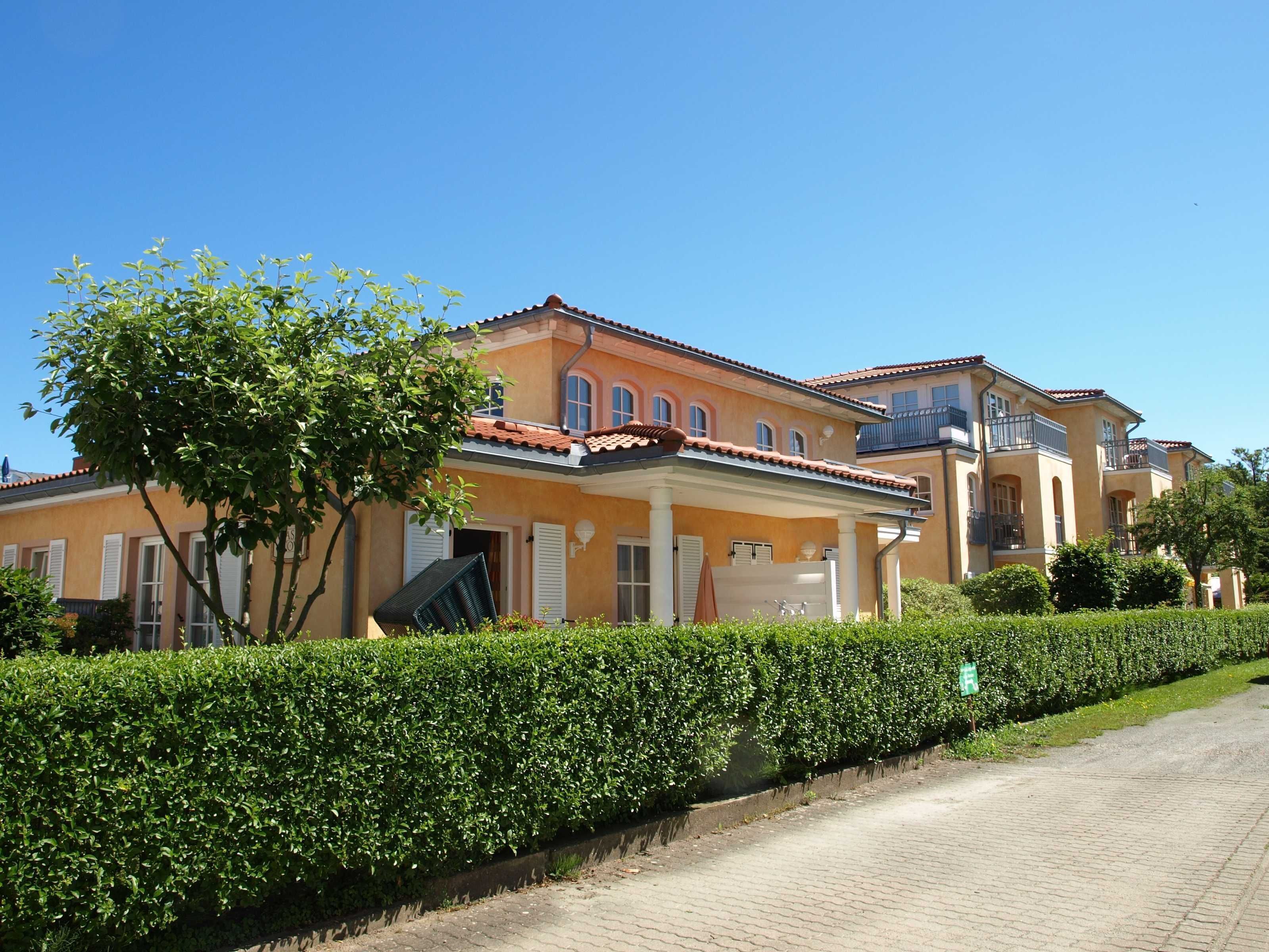 A row of Mediterranean-style houses with a paved driveway and well-maintained hedges.
