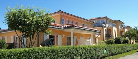 A row of Mediterranean-style houses with a paved driveway and well-maintained hedges.