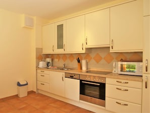 Una cocina compacta con gabinetes blancos, horno Bosch, microondas y cafetera.