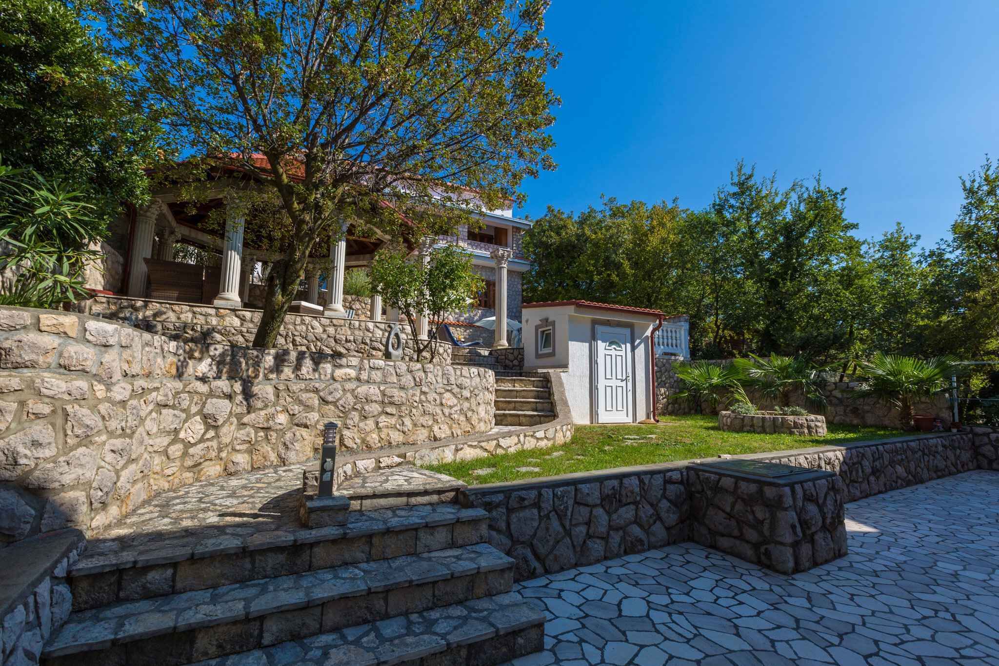 A stone staircase leading to a building with a white facade and columns, surrounded by greenery and a clear blue sky.