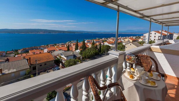 Un balcón con una mesa dispuesta para el té, con vistas a un pueblo costero y al mar.