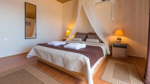 Un dormitorio con cama a dosel, dos lámparas de noche, una mesita de noche y un aire acondicionado de pared.