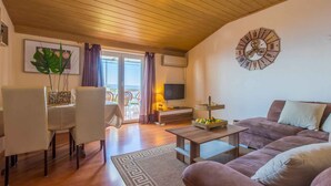 Una sala de estar con techo de madera, un reloj de pared redondo, un televisor, un sofá, una mesa de centro y un comedor con sillas y una mesa.