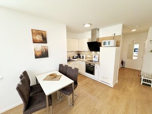 Une cuisine compacte avec des meubles blancs, un four à micro-ondes et une cuisinière. On y trouve également un coin repas avec une table blanche et des chaises marron.