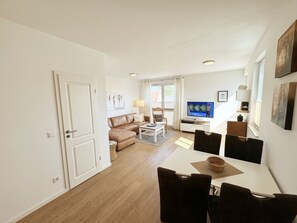Un salon moderne avec un canapé, une table basse et un téléviseur. Il y a également un coin repas avec une table et des chaises.