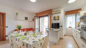A dining area with a table set for two, a kitchen with a microwave and stove, and a TV in the background. - Holiday apartment with balcony and air conditioning (Alghero)