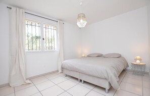 Ein Schlafzimmer mit einem Bett, zwei Nachttischlampen, einer Chandelierleuchtre und einem Fenster mit Vorhängen.