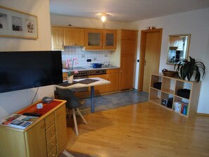 A compact kitchen with wooden cabinets, a dining table, a TV, and a bookshelf. - Apartment Brinkmann (Clausthal-Zellerfeld)