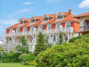 Un hôtel à plusieurs étages, doté de balcons, d’un toit recouvert de tuiles rouges et d’une végétation luxuriante au premier plan.