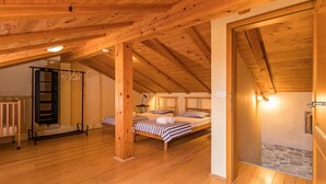 Une chambre mansardée chaleureuse avec des poutres en bois, deux lits, une échelle et un mur en pierre.
