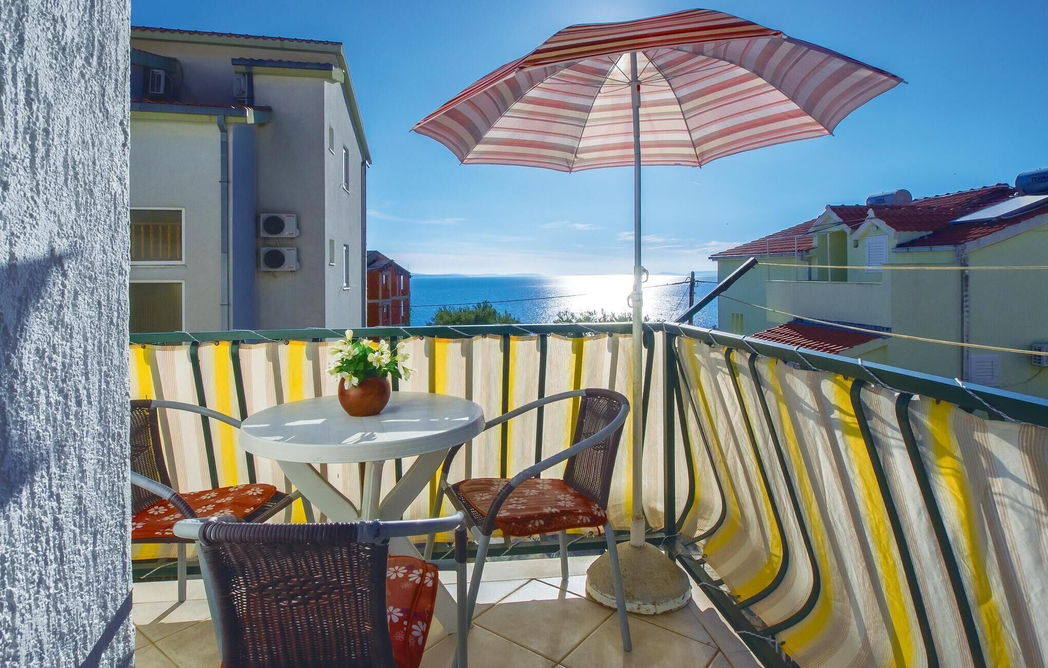 Un balcone con tavolo, sedie, un ombrellone a righe e vista sul mare.
