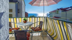 Ein Balkon mit Tisch, Stühlen, einem gestreiften Sonnenschirm und Blick auf das Meer.