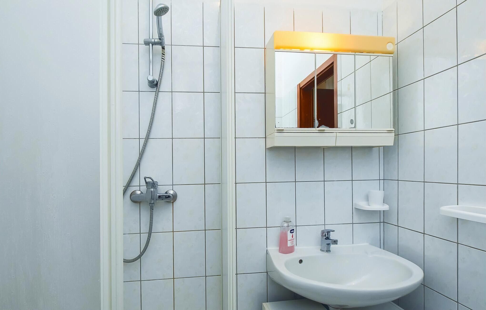 Een badkamer met douche, wastafel en spiegel.
