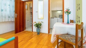 Ein Zimmer mit Holzboden, einem Esstisch mit weißer Tischdecke, einer Vase mit Blumen und einem Stuhl.