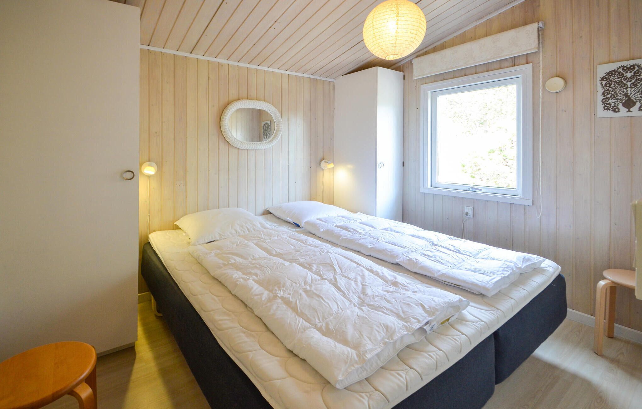 Une chambre avec un grand lit, des murs en bois, une fenêtre et un miroir rond.