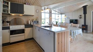 A kitchen with a central island, a stove, and a microwave. There is a dining area with a table and chairs. - 4 bedroom lovely home in Thisted (Thisted)