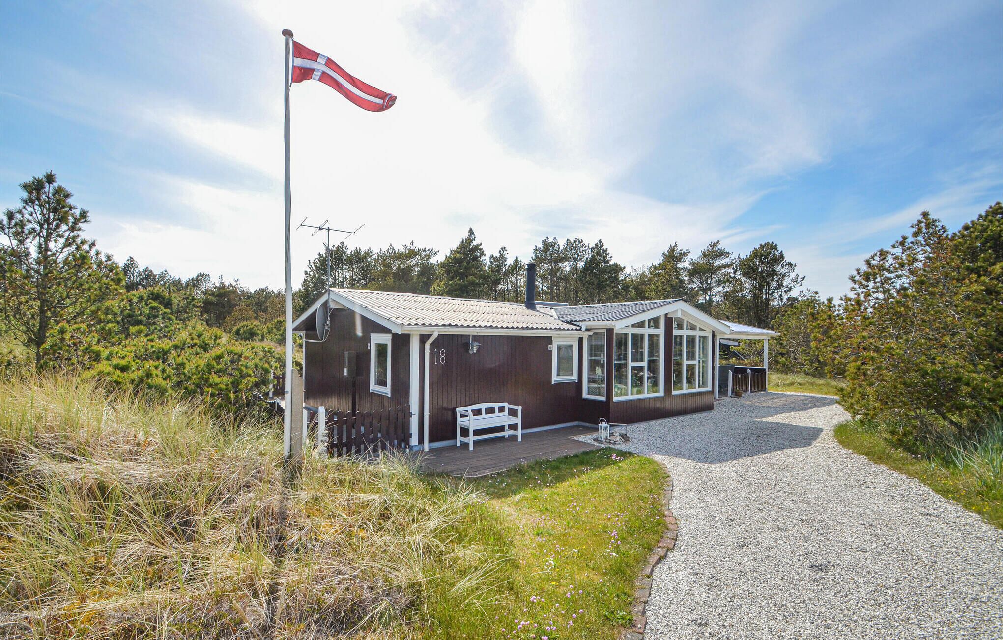 Een houten vakantiehuis met veranda, vlag en een grindpad.