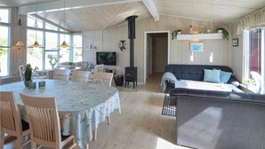 A spacious living area with a large sofa, a dining table with chairs, a TV mounted on the wall, and a fireplace. - 4 bedroom lovely home in Thisted (Thisted)