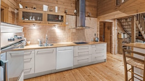Cocina moderna con paredes de madera, estufa de acero inoxidable, lavavajillas y comedor de madera con una silla.