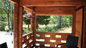 Una cabaña de madera con un porche, una cesta de flores colgante y vistas del entorno cubierto de vegetación.