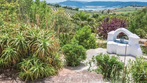 Un jardín con una fuente blanca, diversas plantas y vistas a colinas distantes.