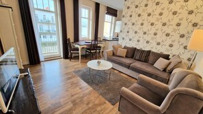 Un salon comprenant un canapé, un fauteuil, une table basse, un téléviseur, une table à manger, des chaises et une vue sur l’extérieur.