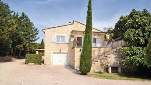 Una casa de piedra con puerta de garaje blanca, una escalera que lleva a un balcón y un árbol alto y delgado al frente.