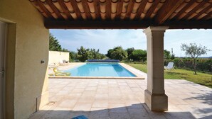 Un área de piscina al aire libre techada con una pérgola, un patio de piedra y vistas al follaje circundante.