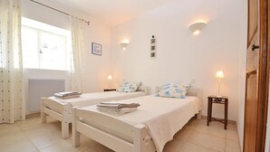Un dormitorio con dos camas individuales, una mesita de noche pequeña con lámpara y una ventana con cortinas.