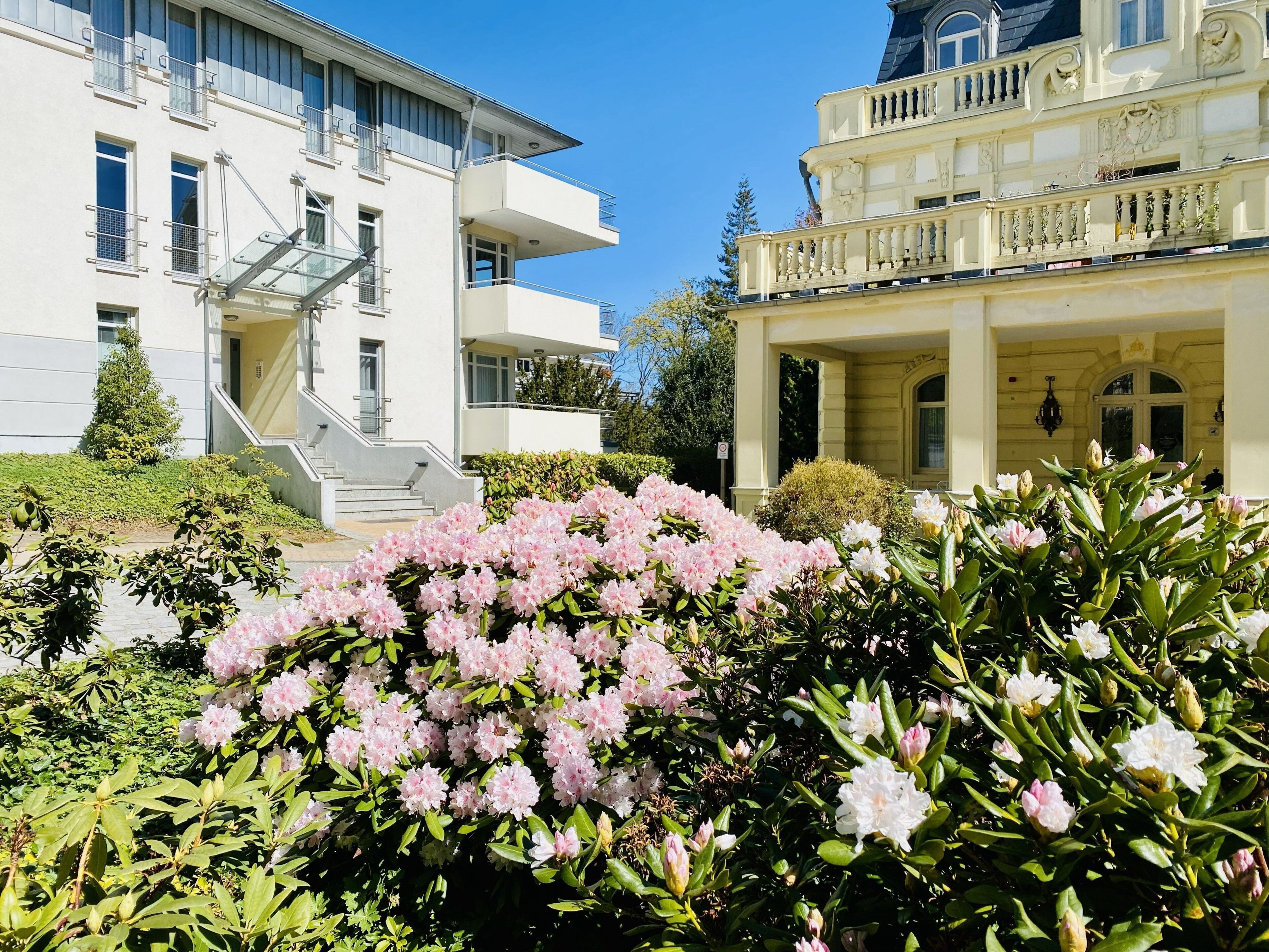 A building with a staircase, a balcony, and a garden with pink flowers.