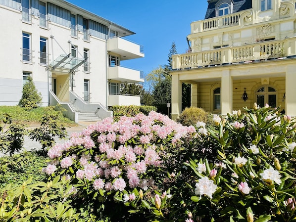 A building with a staircase, a balcony, and a garden with pink flowers.