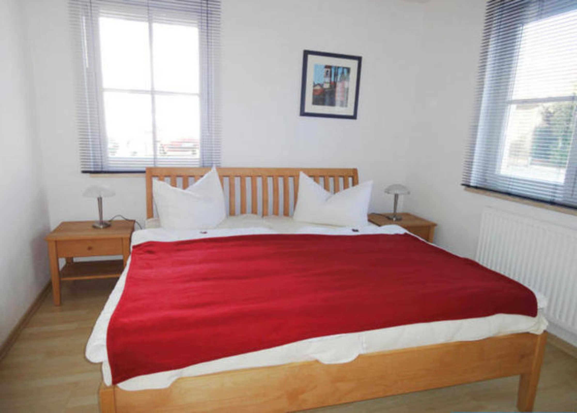 A bedroom with a wooden bed, white bedding, two bedside tables, and a framed picture on the wall.
