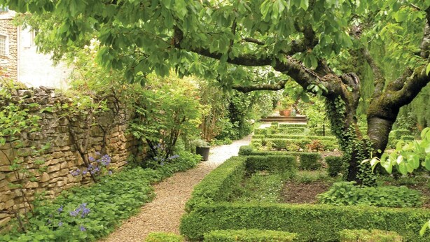 Un jardí amb mur de pedra, camí de grava i guals ben tallats.