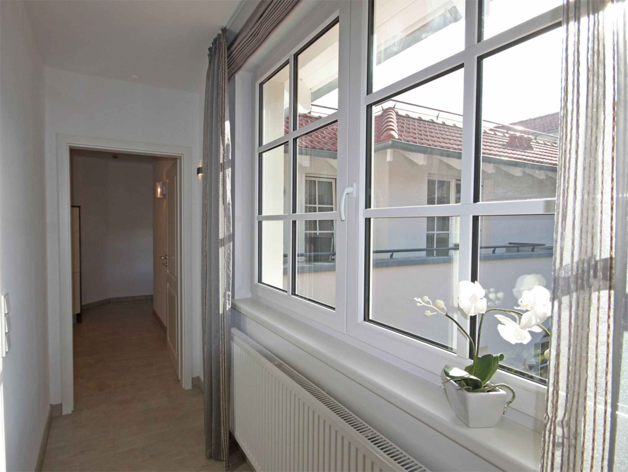 A corridor with a radiator, a potted orchid, and a window with a view of a building with a red roof.