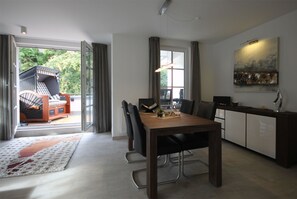 Un espace repas moderne avec une table en bois, des chaises noires et une vue sur un balcon agrémenté d’un canapé et d’une fenêtre.