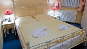 Una cama individual con estructura metálica, una mesita de noche con lámpara y un radiador.